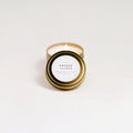 Lit orange and clove soy candle in gold travel tin with white label on white background