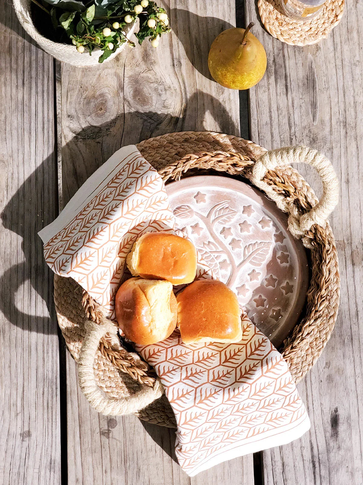 Woven basket with rope handles holding a ceramic plate and three bread rolls on a wooden table