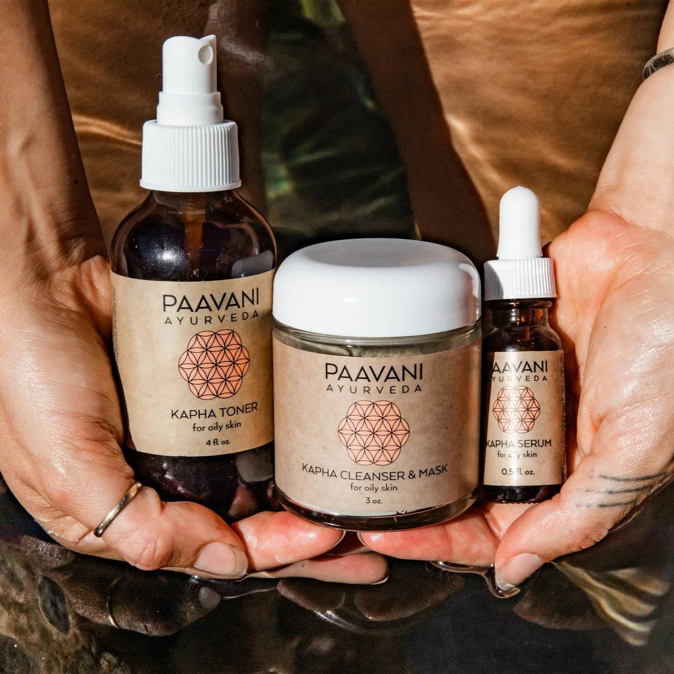 Hands holding PAAVANI Ayurveda Kapha skincare trio—toner, cleanser & mask, and serum—for oily skin.