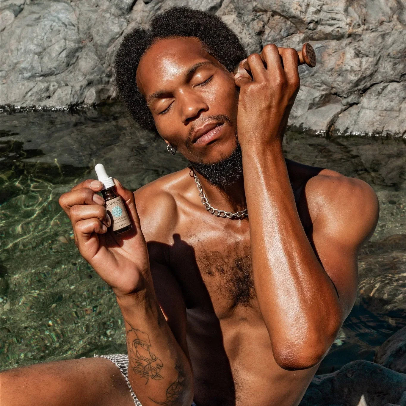 Man by rocky water using facial tool and dropper serum, Qu!rk Boutique wellness skincare