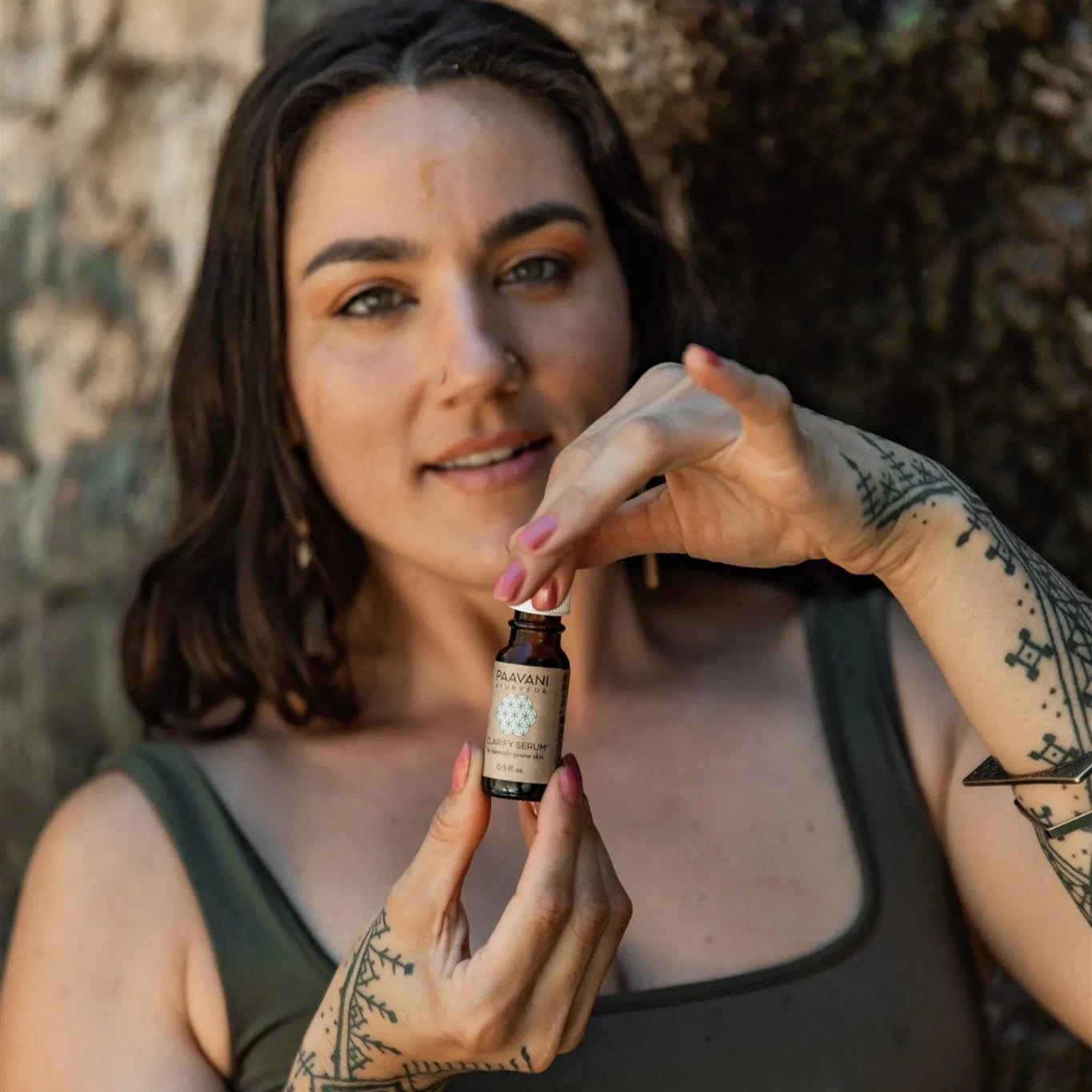 Tattooed woman holding PAAVANI Clarity Serum oil, outdoors, at Qu!rk Boutique gift shop