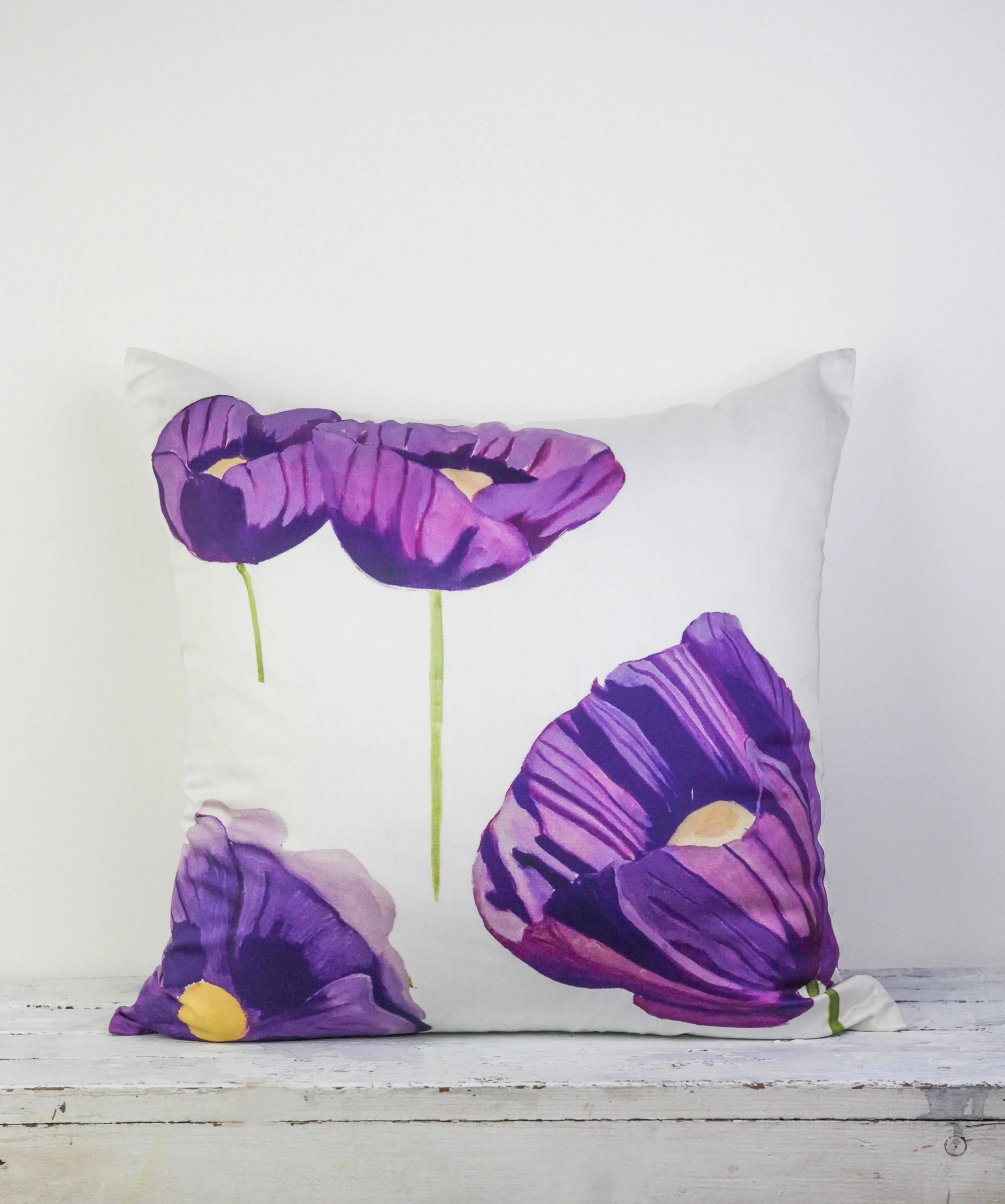White throw pillow with purple poppies floral print on rustic wooden surface