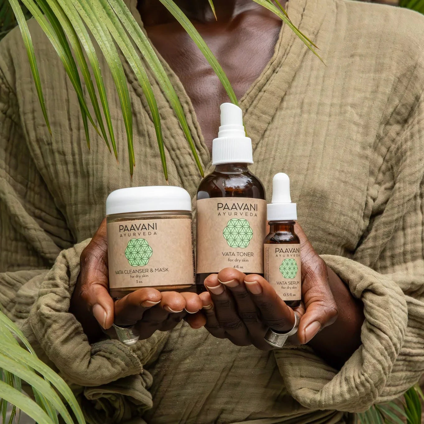 Person in green robe holding Paavani Ayurveda skincare products surrounded by green leaves