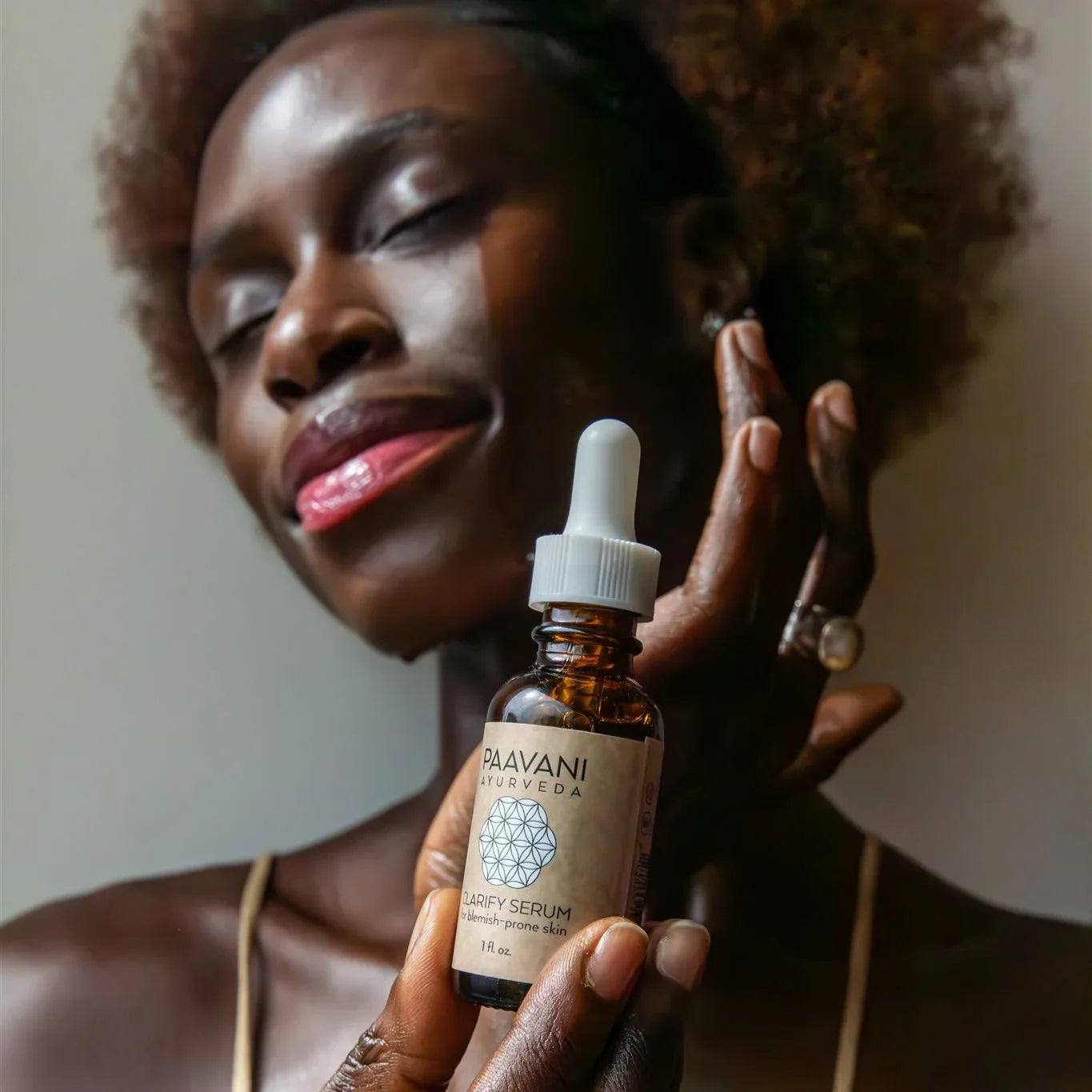 Woman with glowing skin holding Paavani Ayurveda Clarify Serum, boutique skincare product