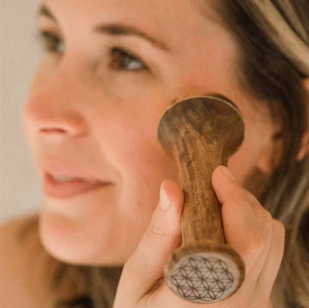 Woman using a wooden facial massage tool with etched geometric design, natural beauty self-care