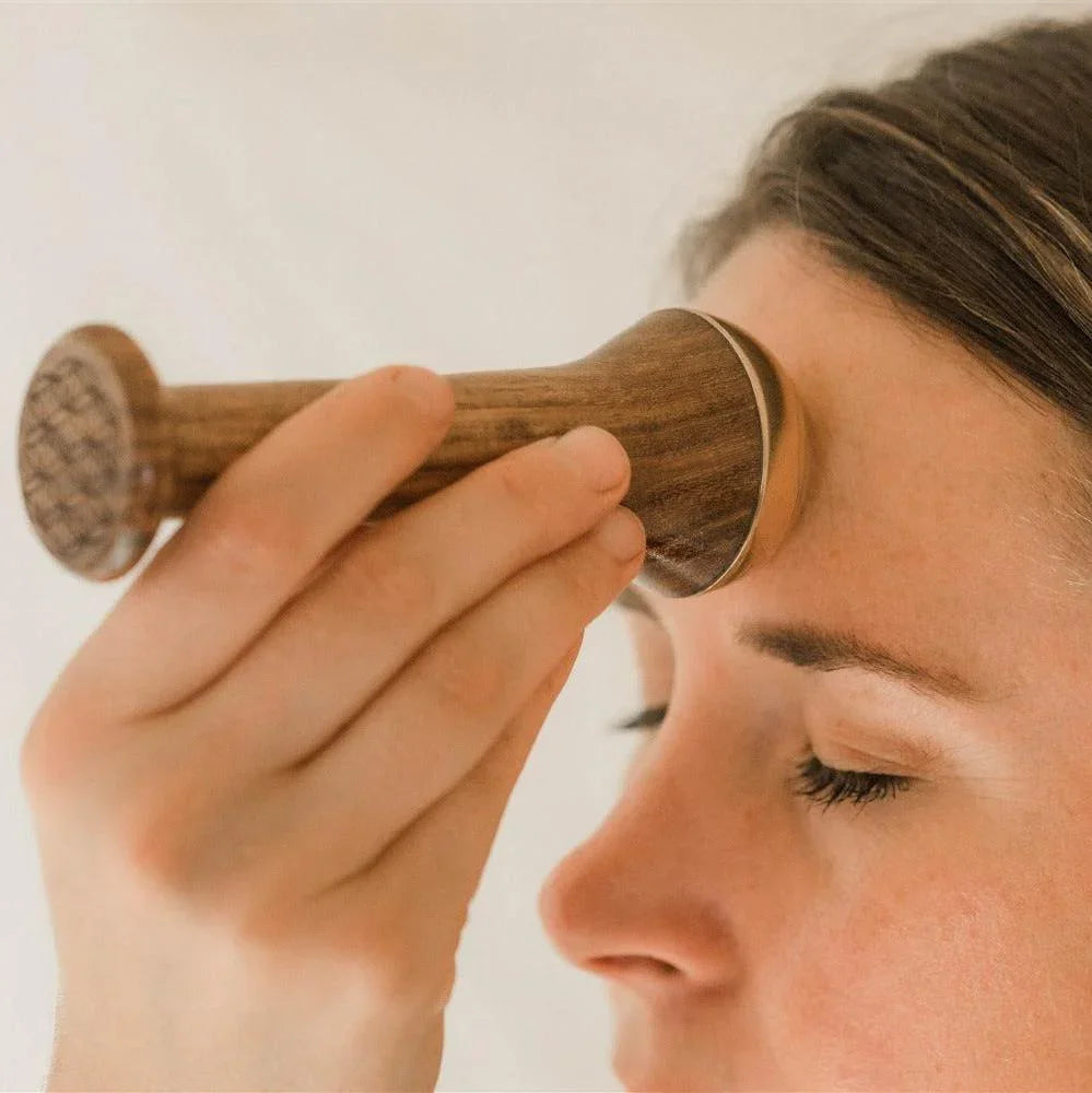 Woman using a wooden facial massage tool on forehead, wellness product at Qu!rk Boutique.