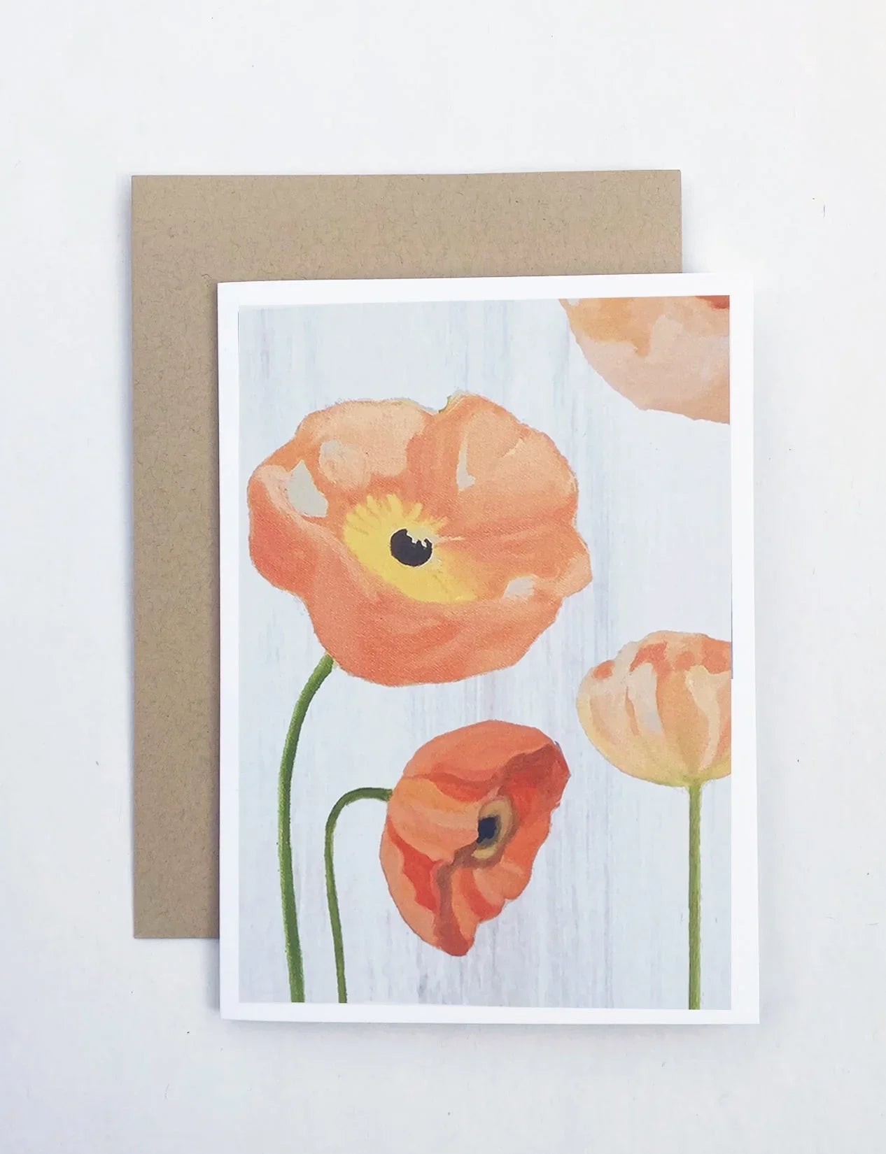 Notecard with peach poppy flowers illustration on a light wood background, paired with a kraft paper envelope