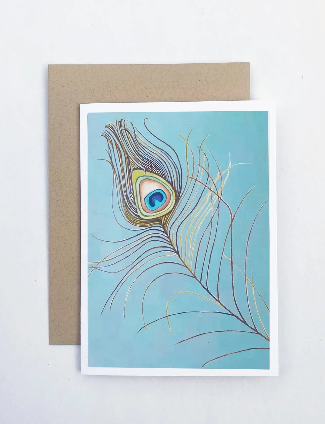 Notecard with a colorful peacock feather illustration on a blue background, next to a brown envelope