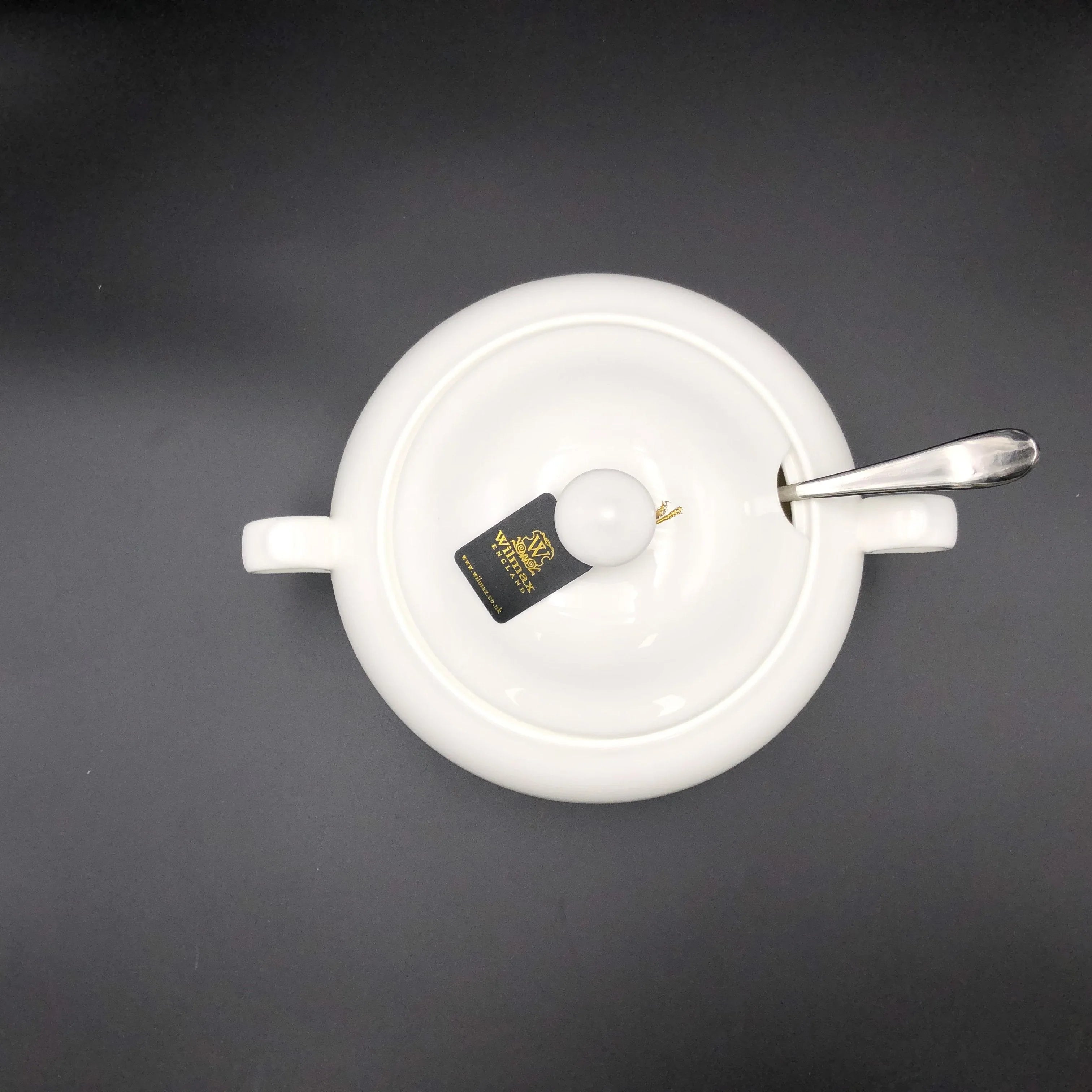 White porcelain sugar bowl with lid, silver spoon, and Verve label on dark background