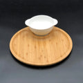 Round bamboo serving board with a white ceramic bowl on black background