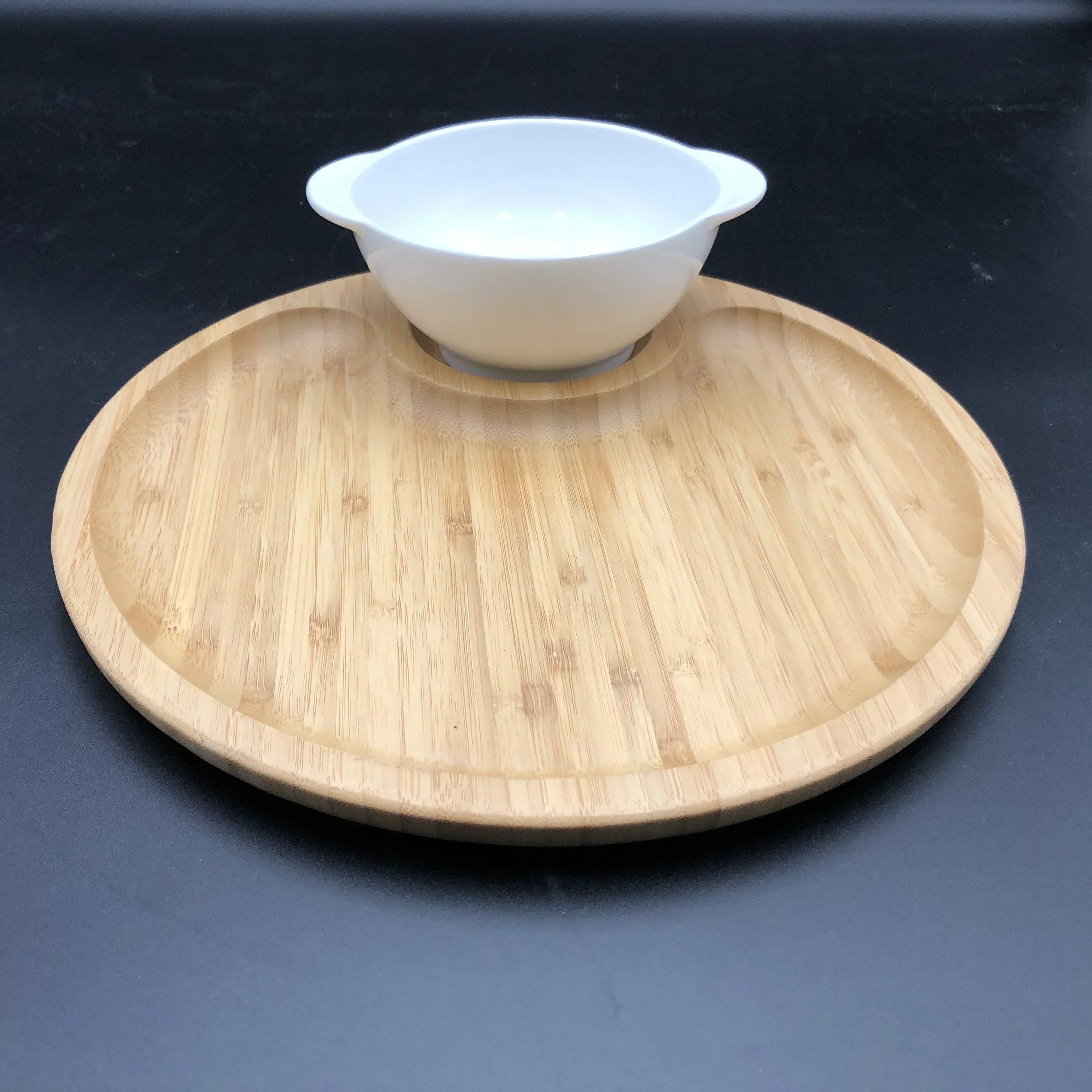 Round bamboo serving tray with integrated white ceramic bowl on black background