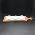 Bamboo serving board with three white ceramic bowls on white rectangular plate against black background