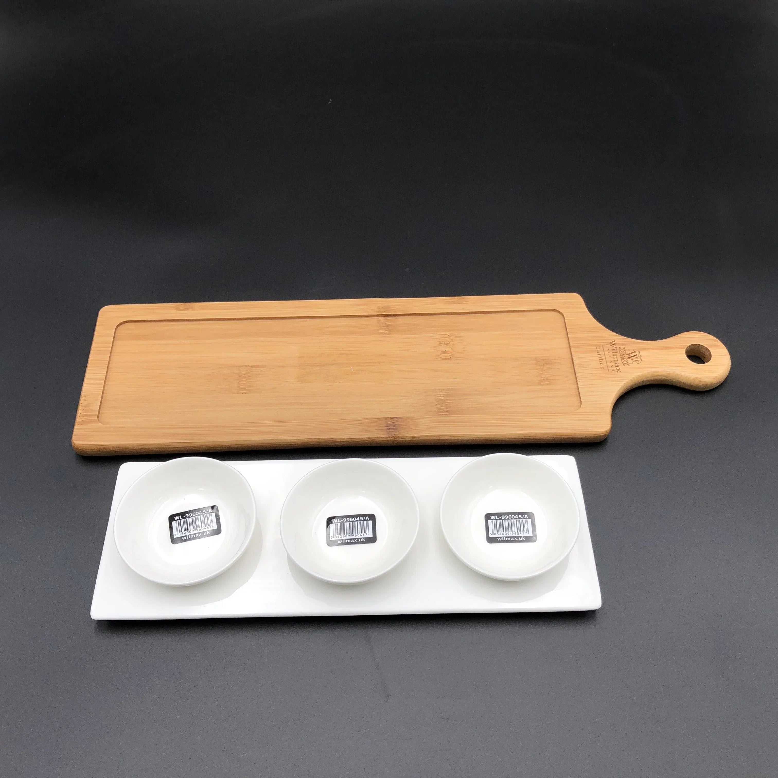 Rectangular bamboo cutting board and white ceramic triple bowl set on black surface