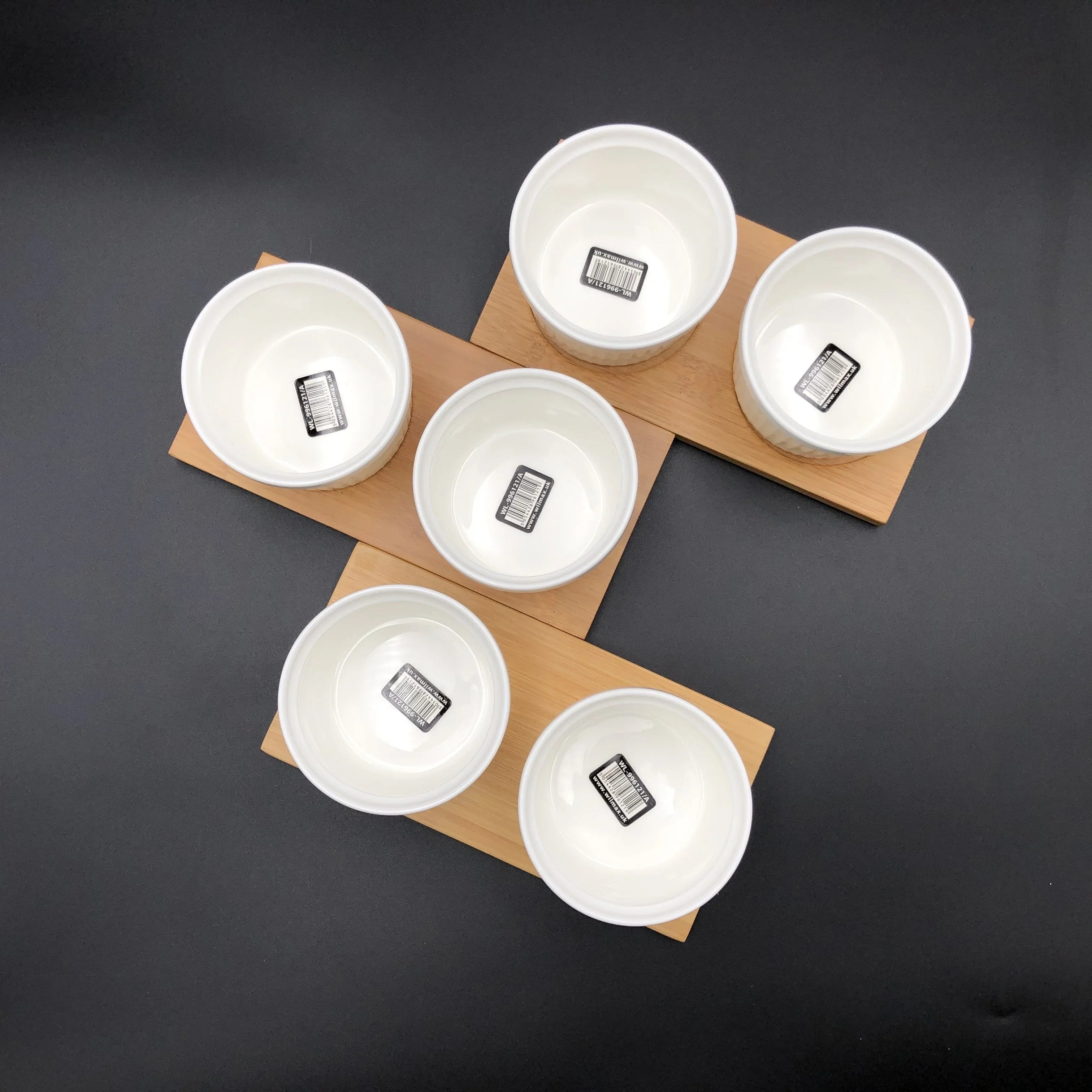 Set of six white ceramic bowls on wooden trays, displayed on a black background
