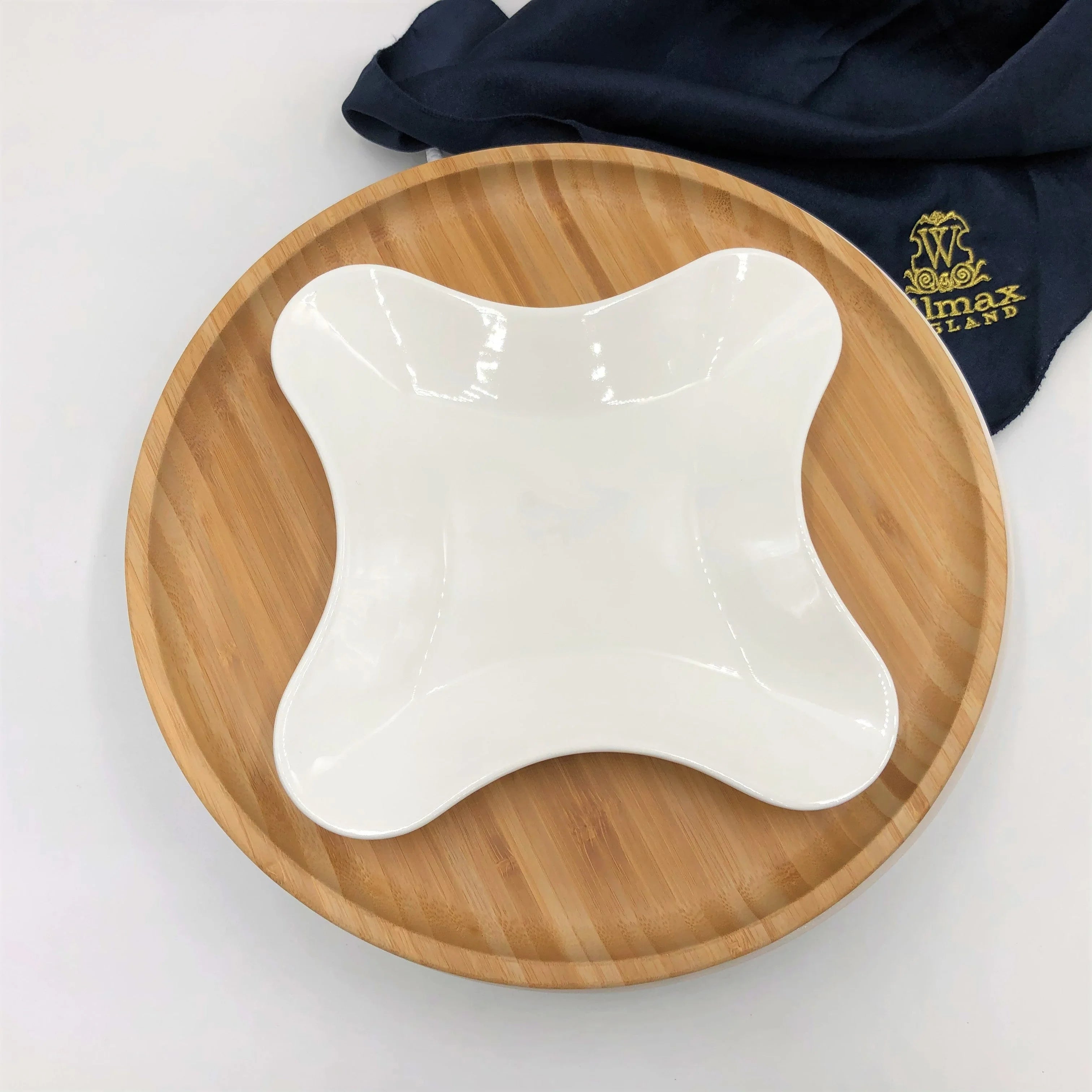 White uniquely shaped ceramic plate on round bamboo serving tray with navy cloth in background