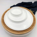 Stacked white ceramic dishes on a round bamboo tray with a dark cloth in background