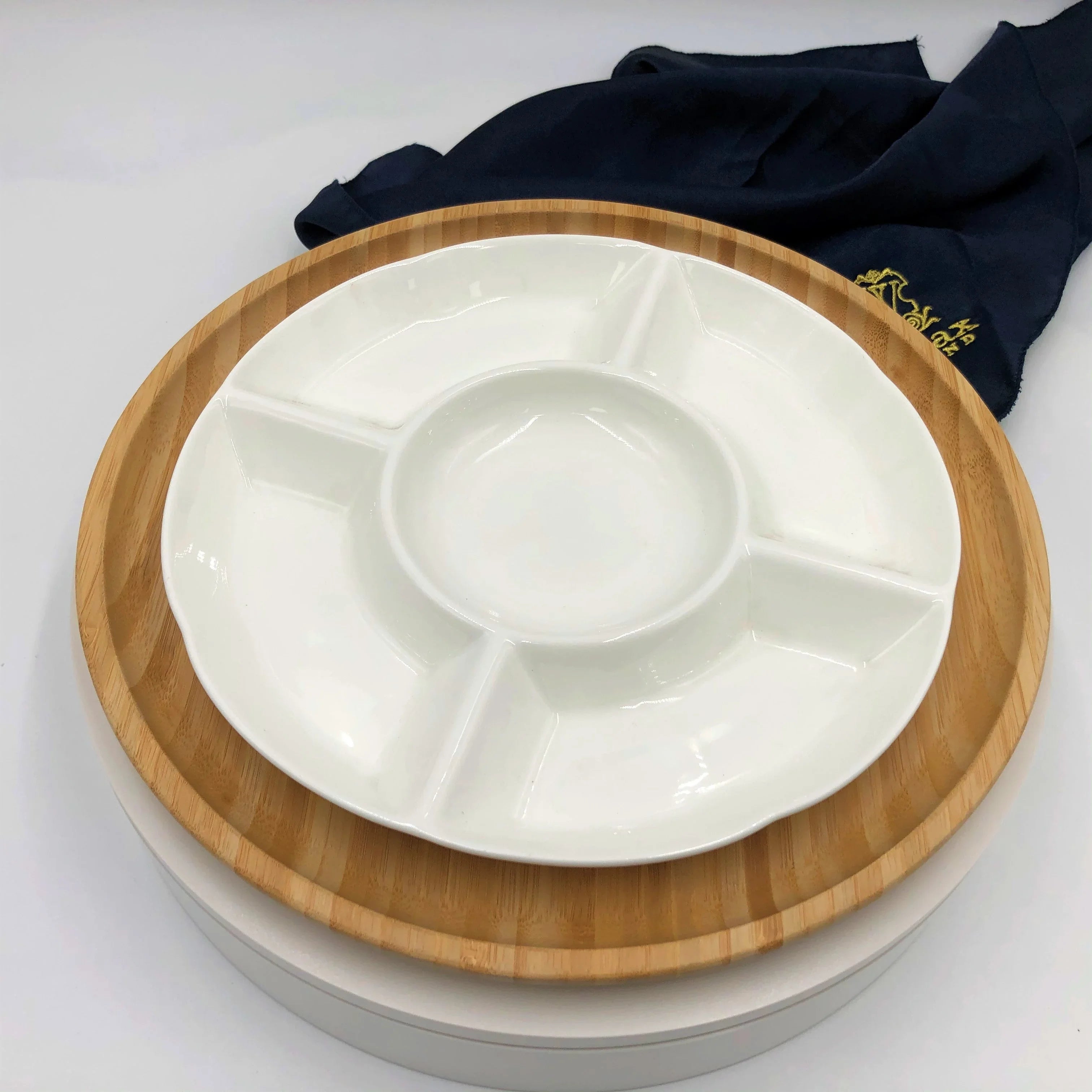 White ceramic divided serving platter on a round bamboo tray with a dark cloth in the background