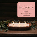 Pillow Talk soy candle in rustic wooden bowl with three flames, greenery, floral scent notes.