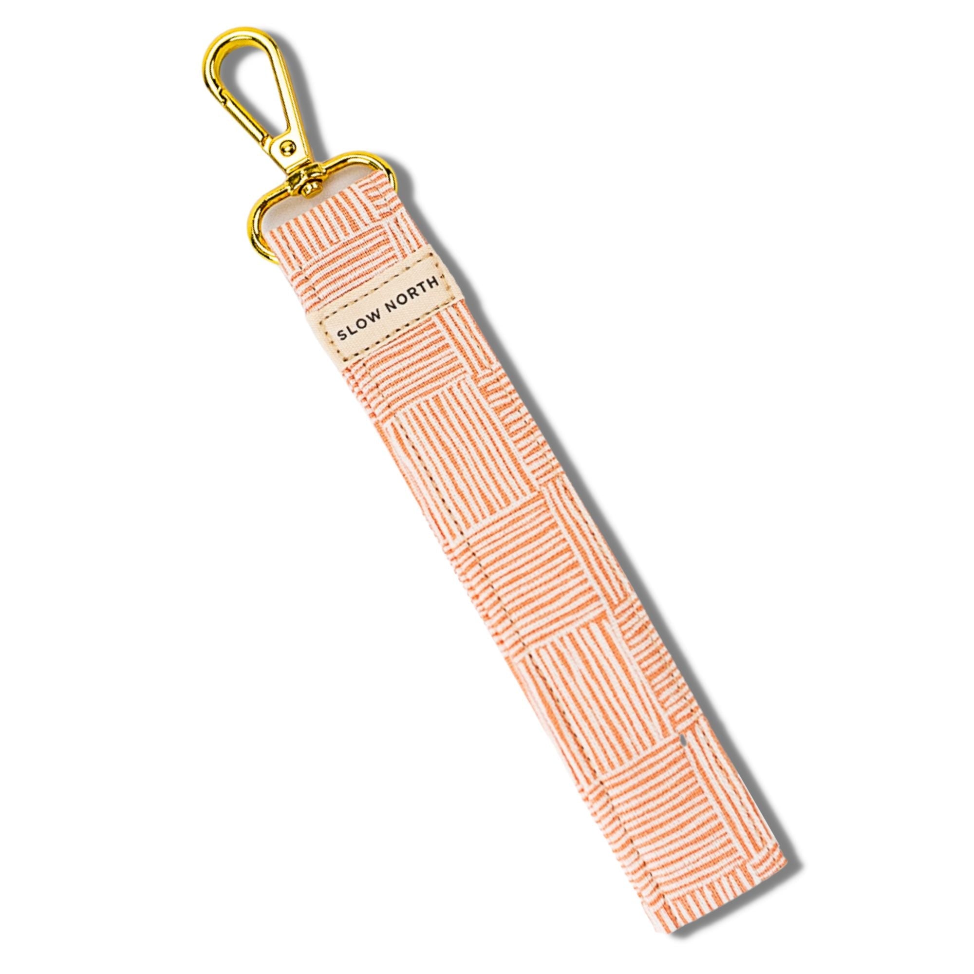 Pink patterned wristlet keychain with gold clasp and slow north label on white background