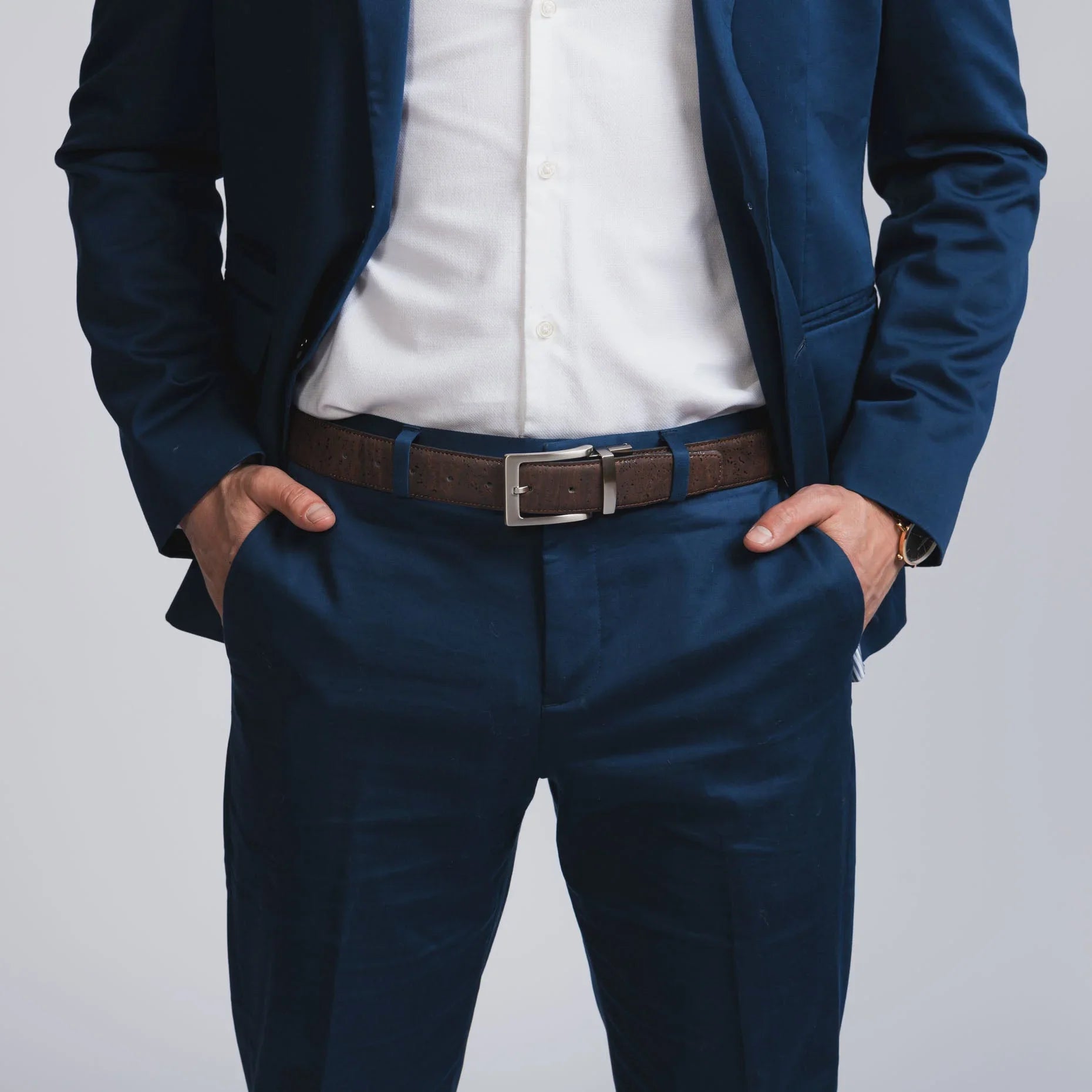 Man in navy blue suit and white shirt with brown belt, hands in pockets, boutique style