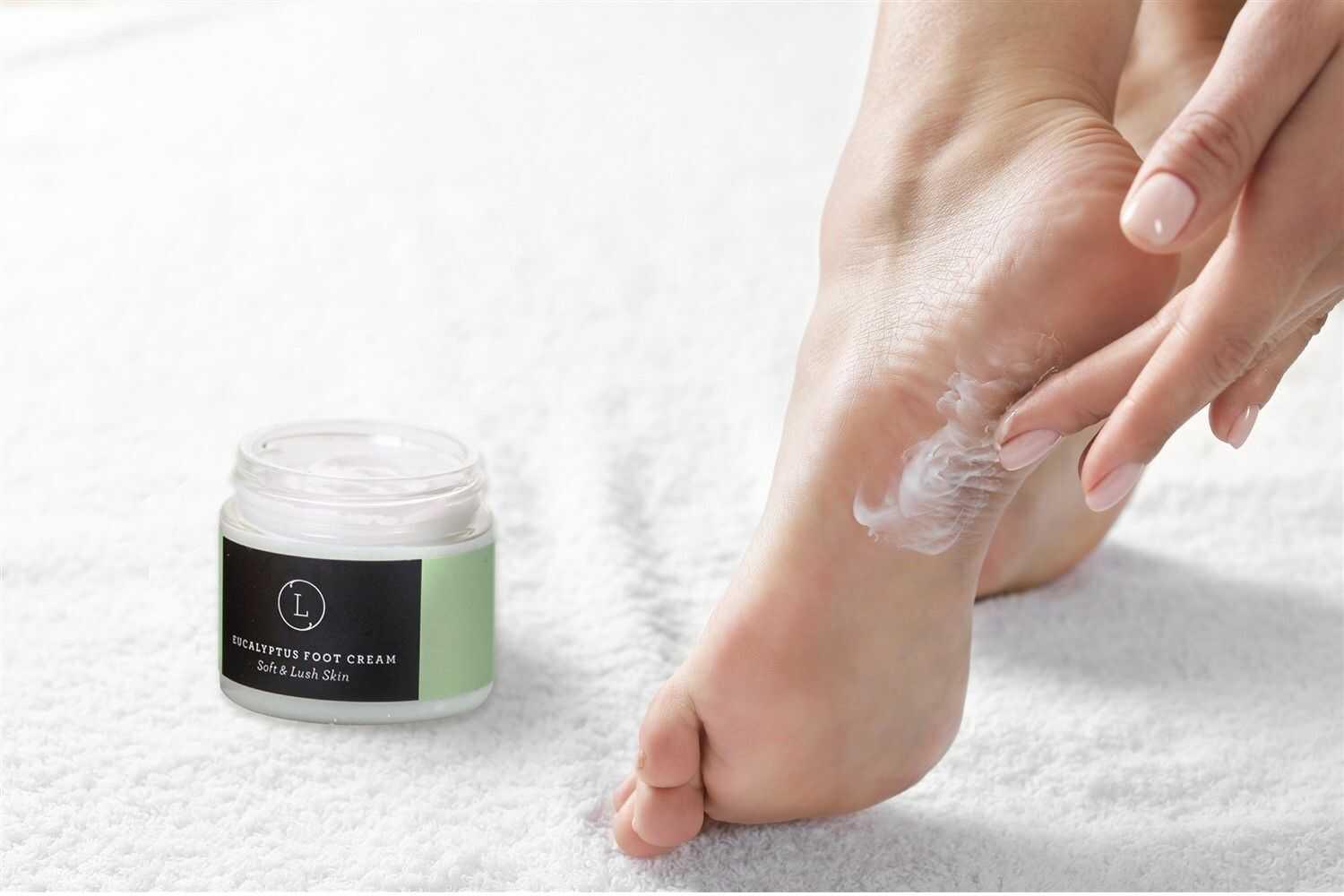 Person applying eucalyptus foot cream on heel with jar of cream on white towel