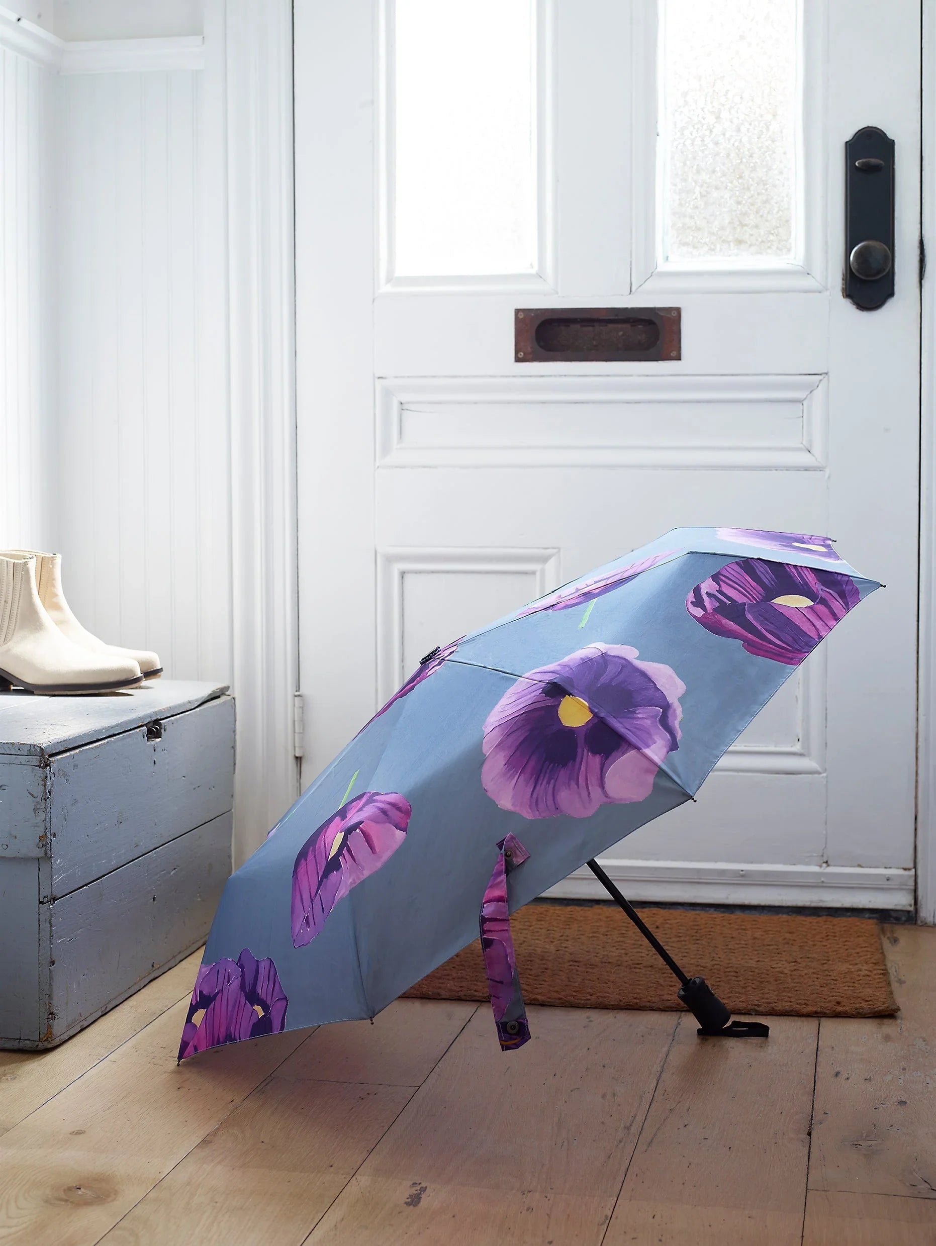 Blue umbrella with large purple poppy flowers on wooden floor by white door