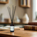 Close-up of amber glass reed diffuser bottle with black reeds on wooden table in cozy room