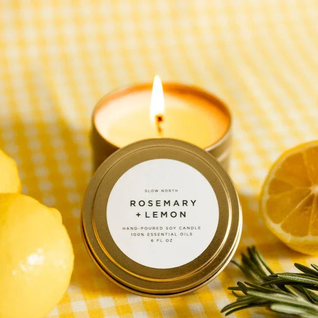 Lit rosemary and lemon soy candle in gold tin on yellow gingham with lemons and rosemary sprigs