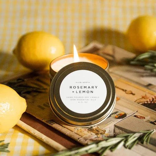 Burning Rosemary Lemon scented soy candle in metal tin with fresh lemons and rosemary on yellow checkered tablecloth