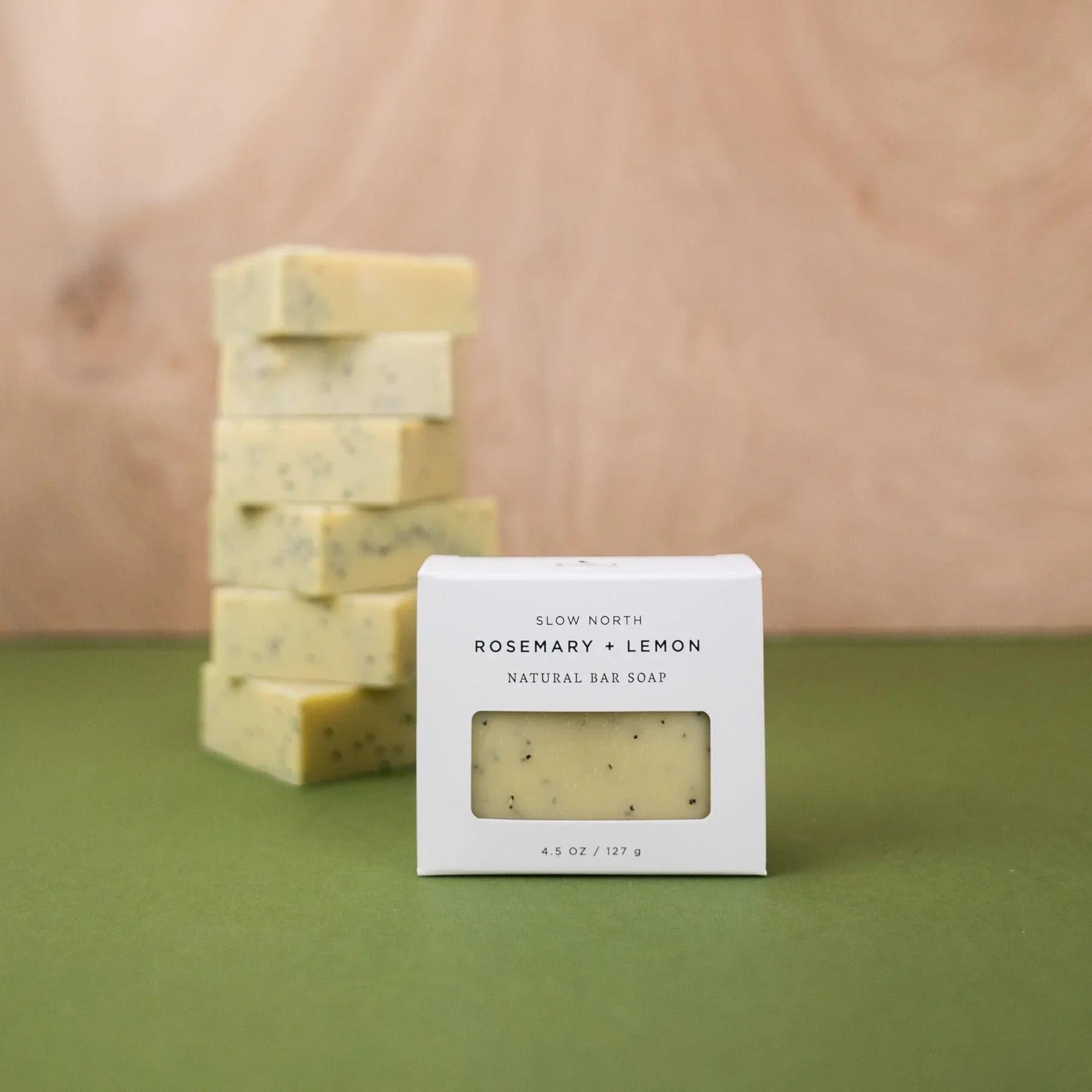 Rosemary and lemon natural bar soap by Slow North on green surface with stacked soap bars in background