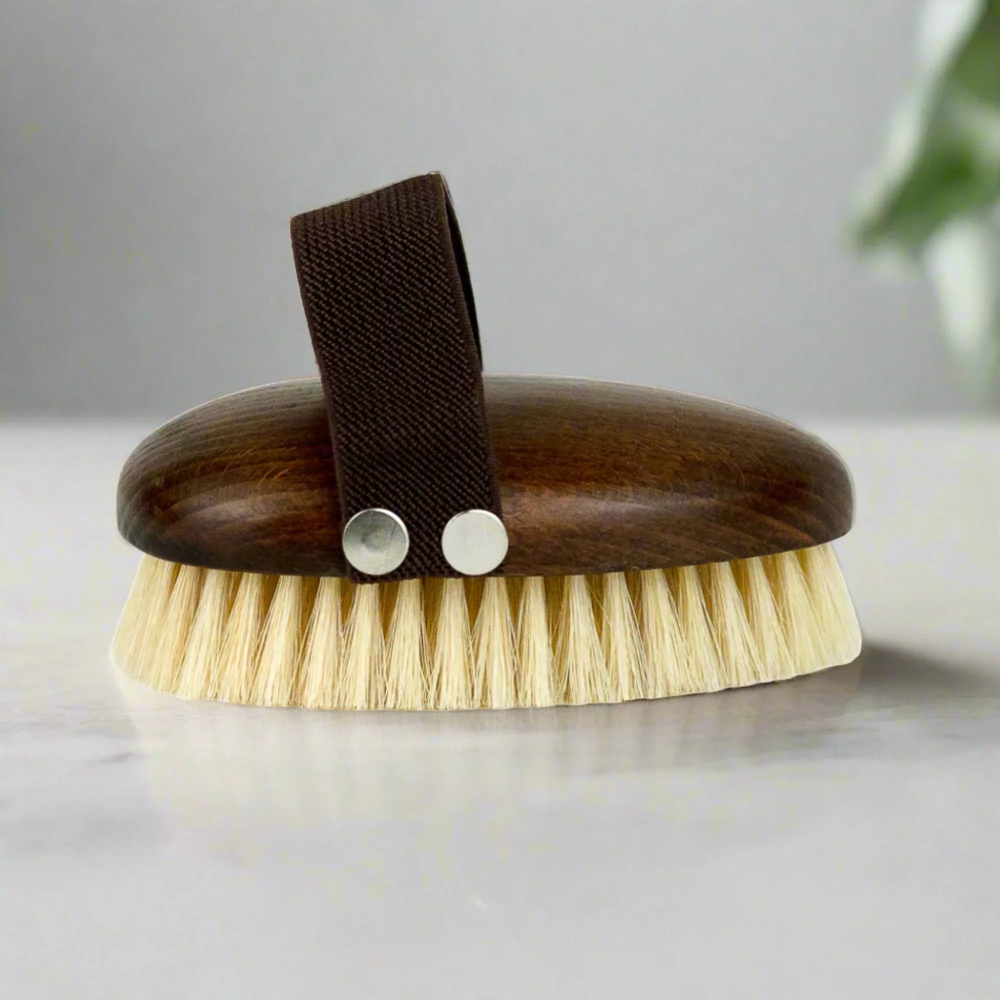 Brown wooden body brush with light bristles and dark fabric handle on marble surface