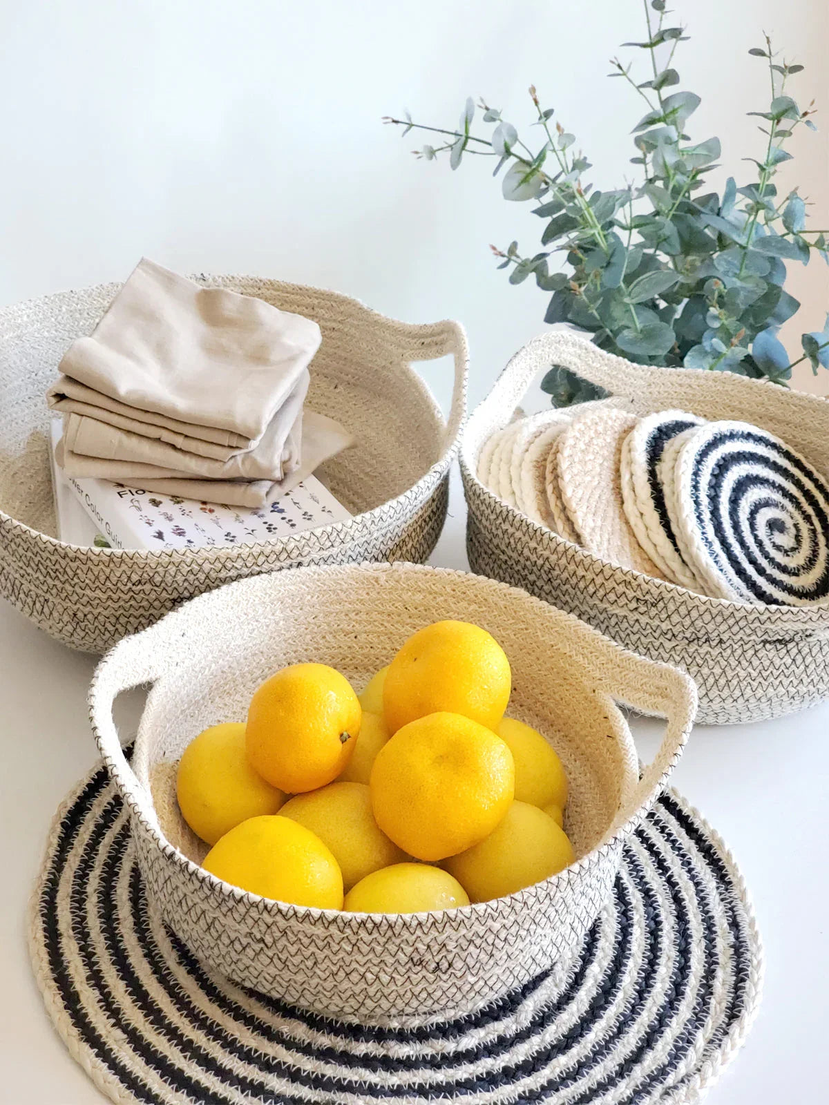 Artist-designed woven rope baskets with yellow lemons, folded linens, spiral mats, and eucalyptus at Qu!rk Boutique.