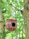 Handwoven colorful acorn-shaped birdhouse hanging from tree branch in lush green forest