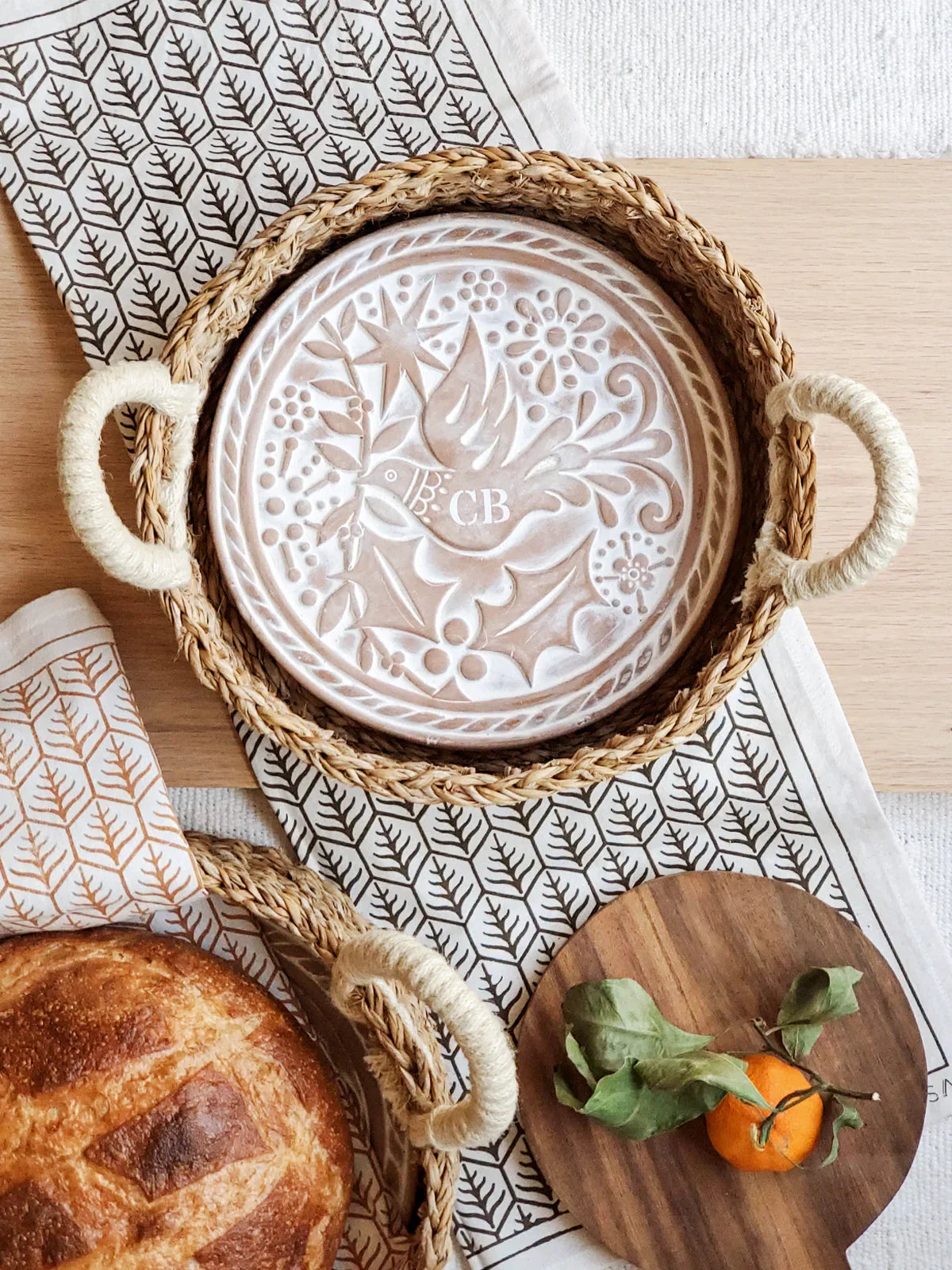 round monogrammed bread warmer basket with bird and floral design on wooden table with bread and mandarin