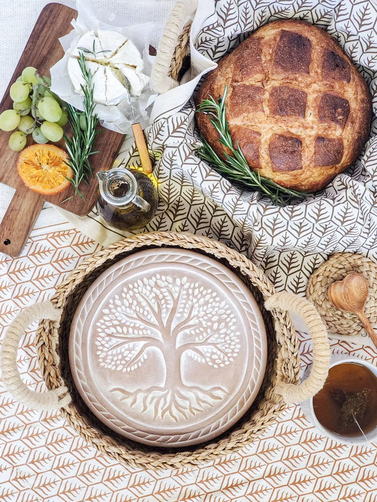 Handcrafted round bread warmer with tree of life design in woven basket, artisan bread, cheese, and tea, Qu!rk Boutique gift idea.