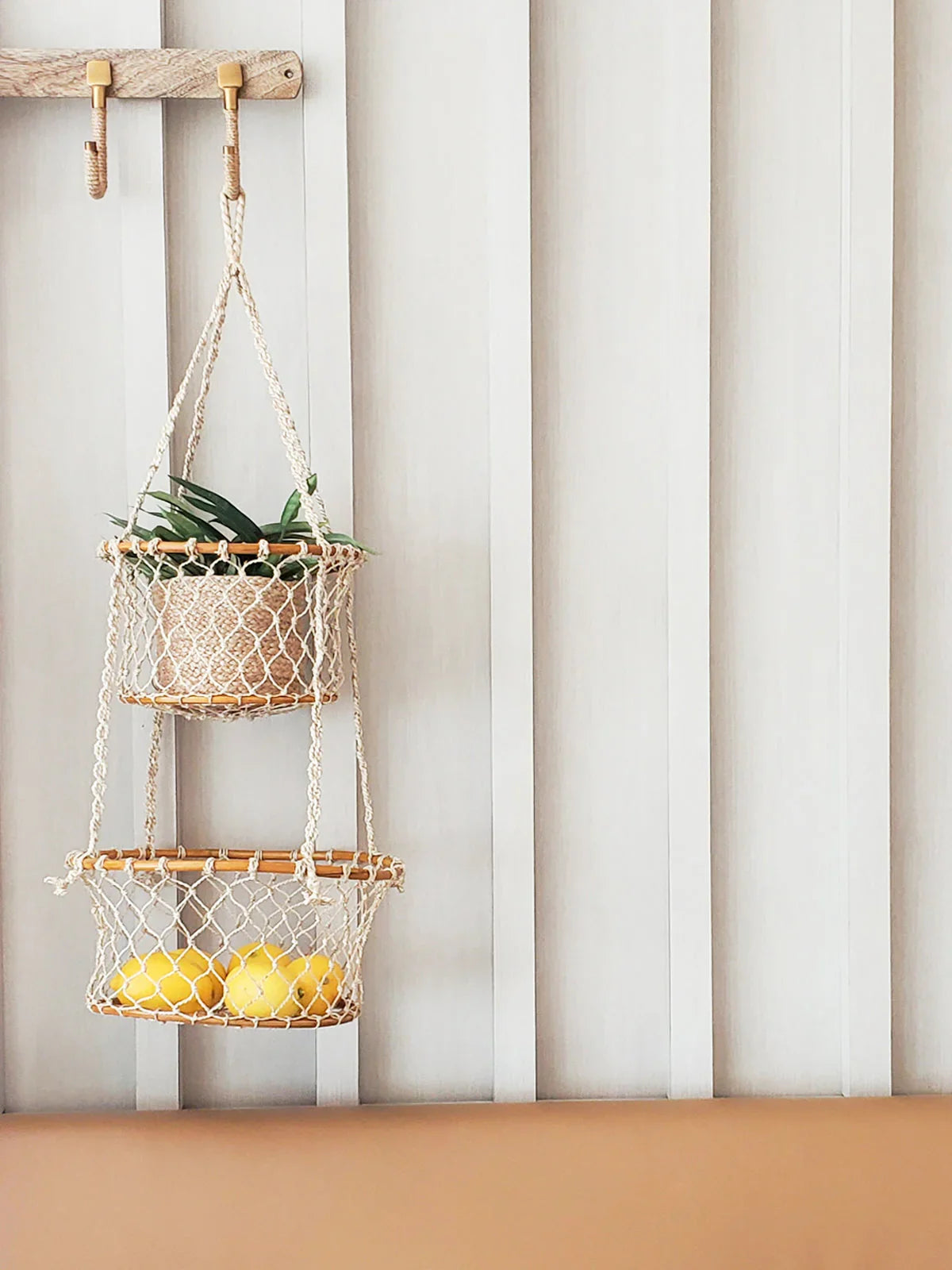 Double hanging macrame basket with lemons and green plant on white wooden wall
