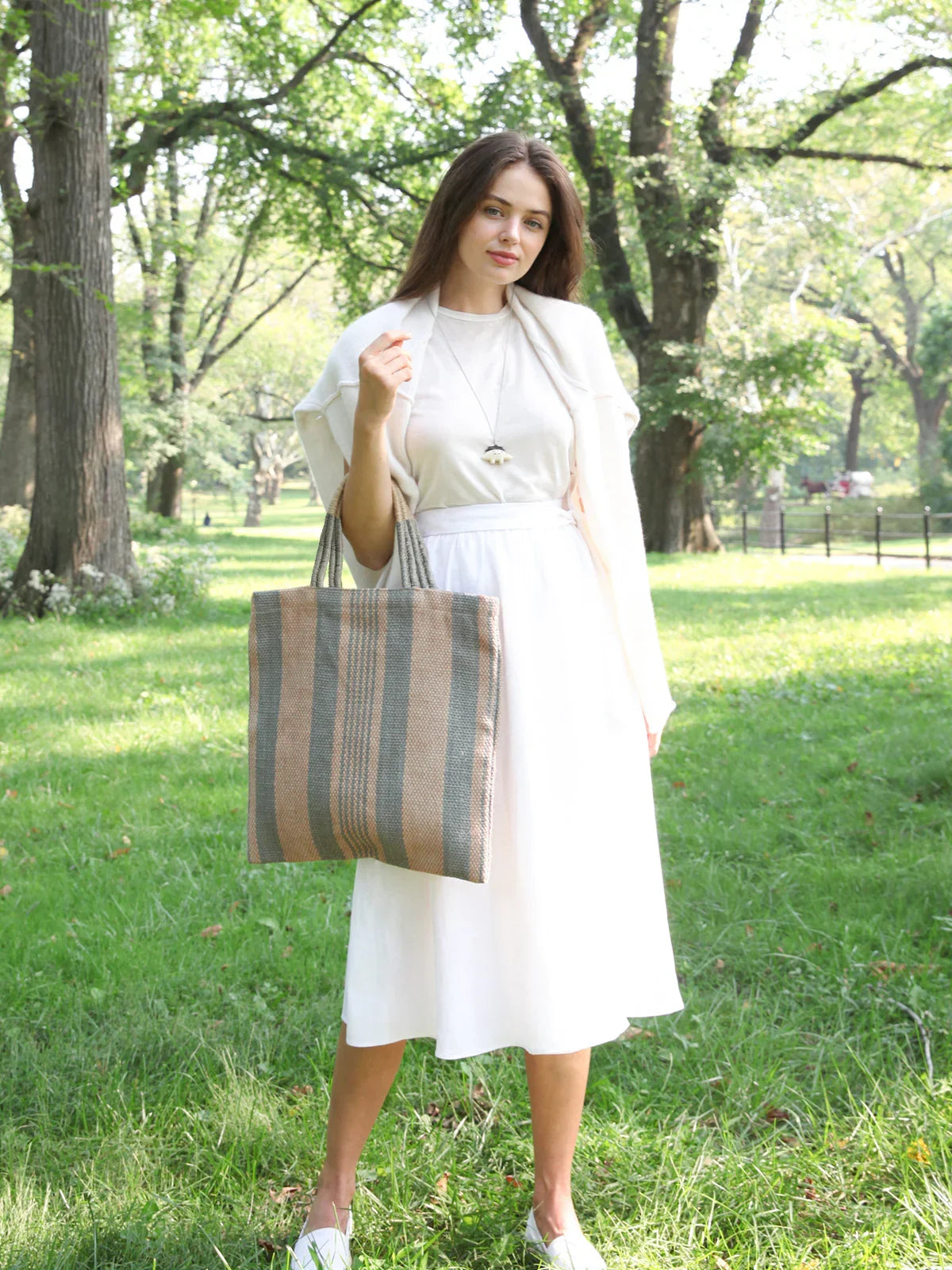 Woman in white dress holding striped jute tote bag in a green park, Qu!rk Boutique