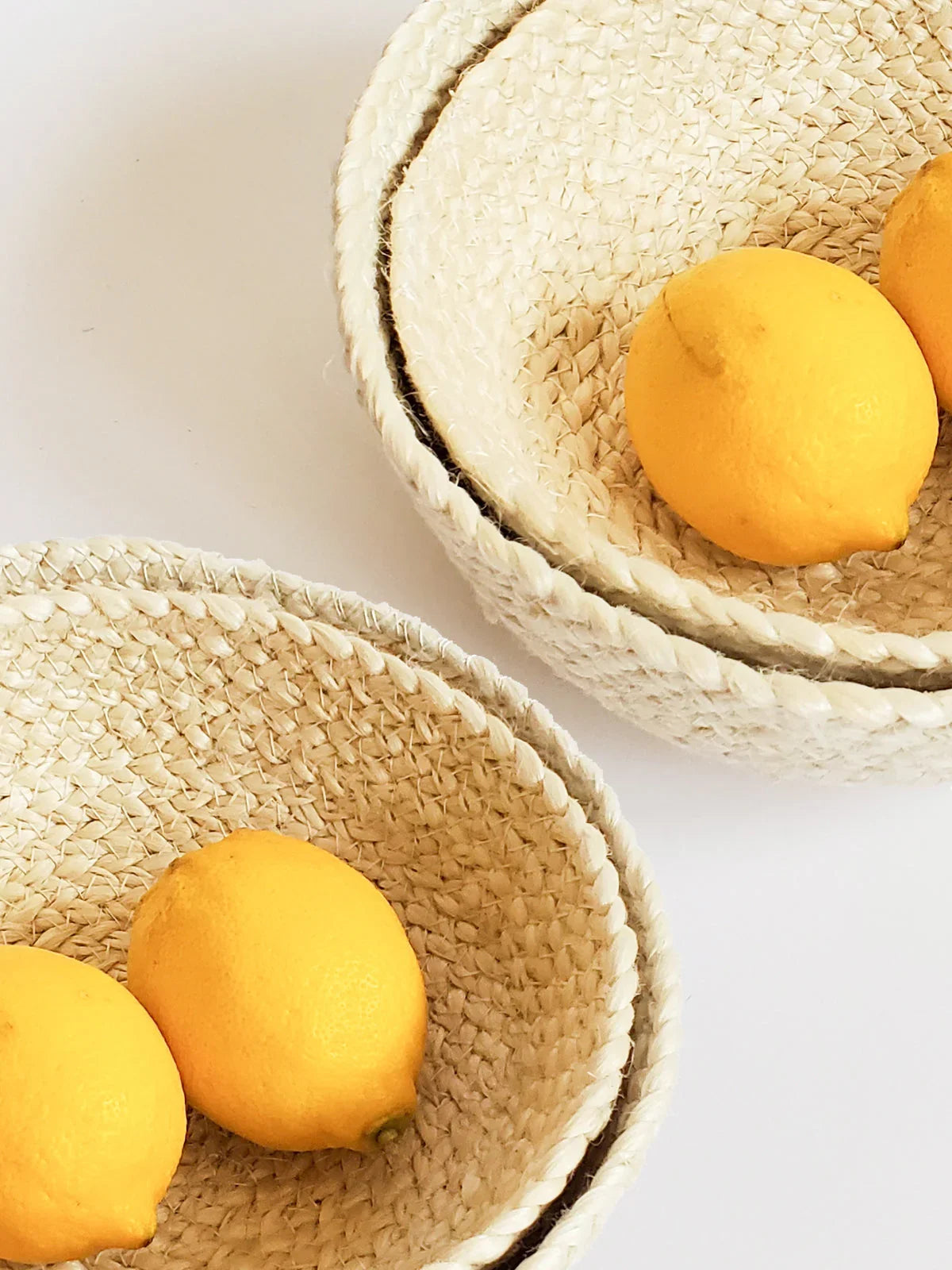Set of four woven white rope bowls with lemons inside on white background