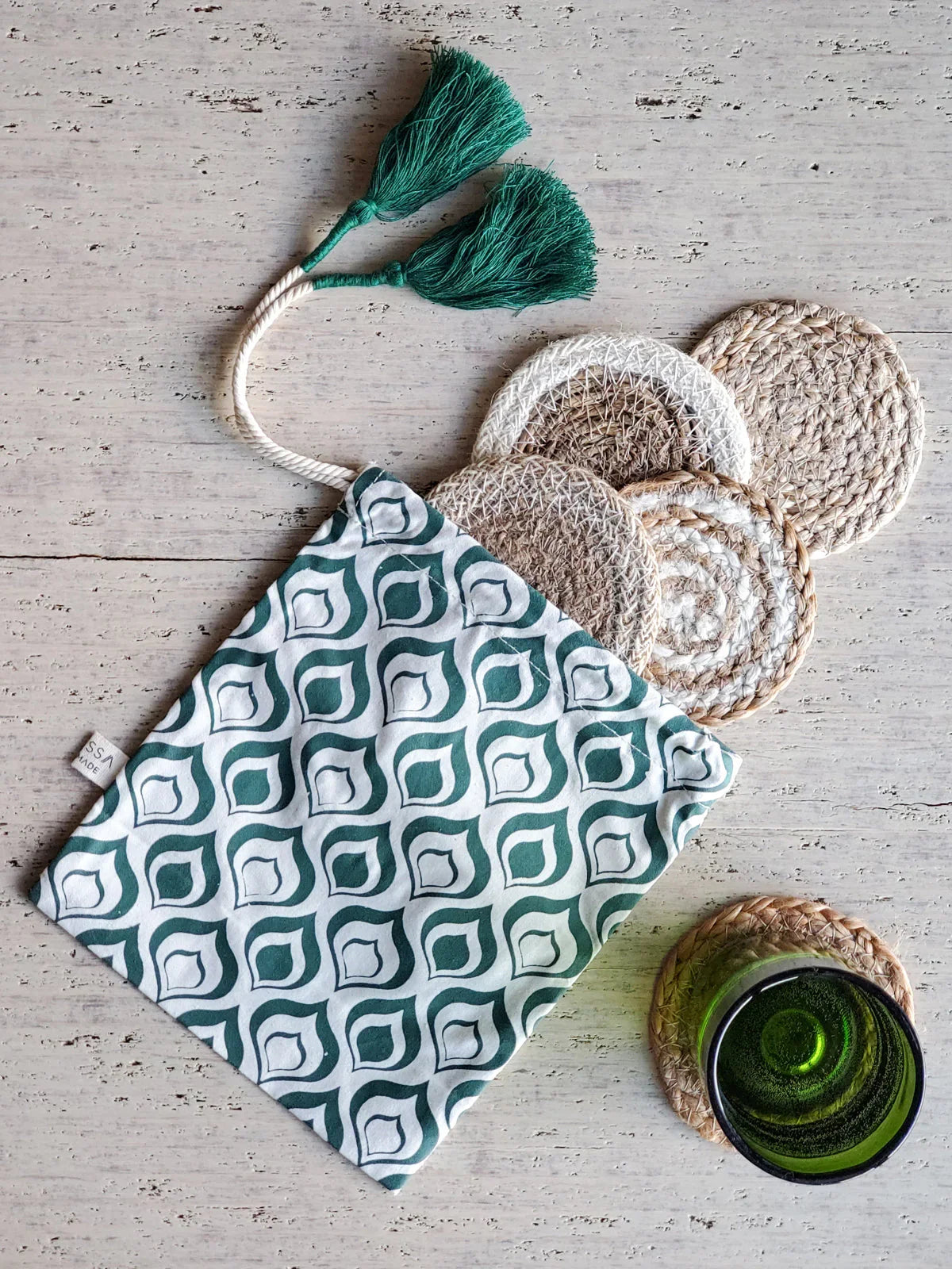 Round woven natural fiber coasters with green patterned pouch and green tassels on light wooden surface