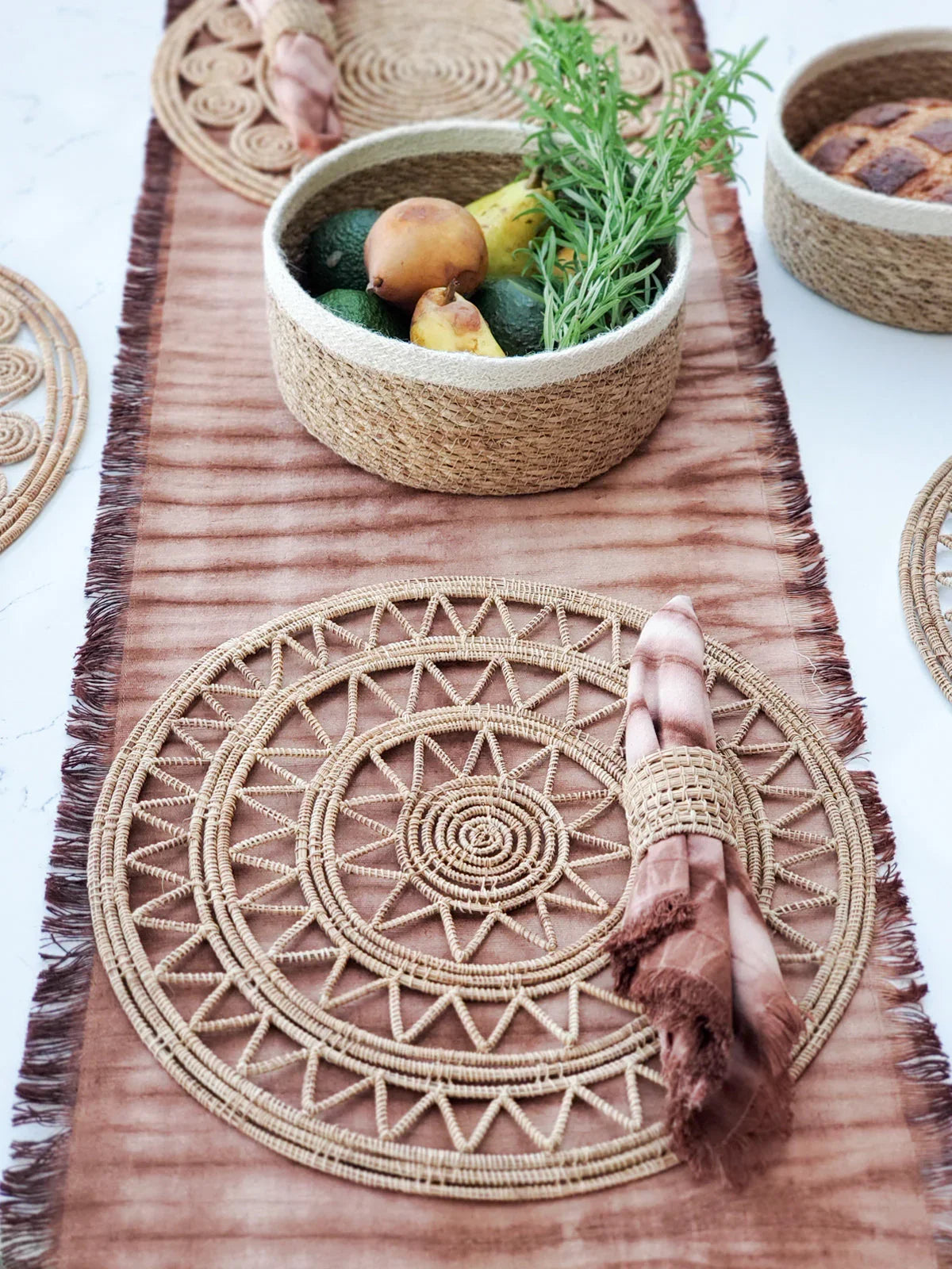 Natural woven placemat with matching napkin ring and pink tie-dye napkin on brown table runner