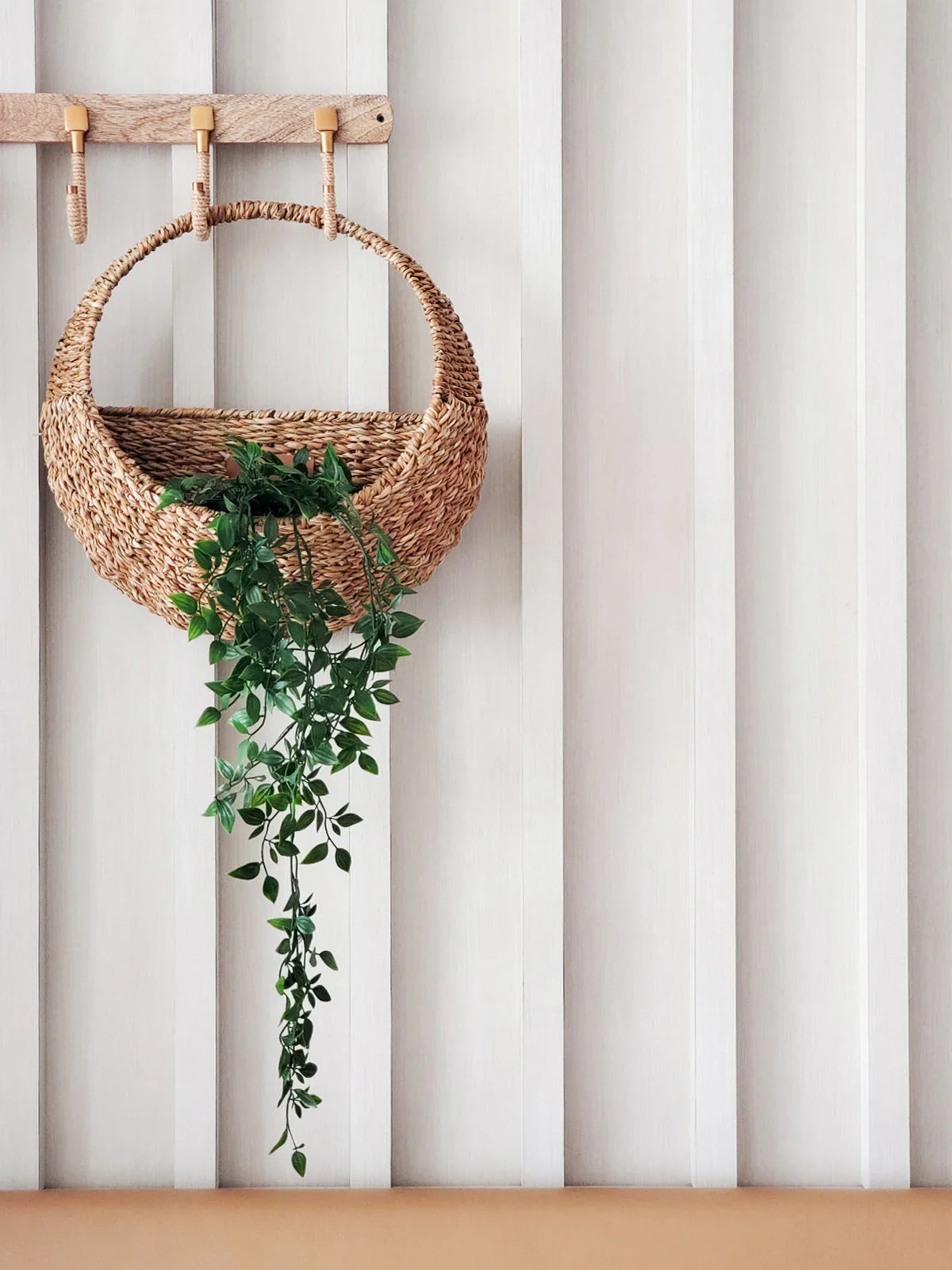 Woven hanging planter with trailing green plant on neutral wall, Qu!rk Boutique home décor.
