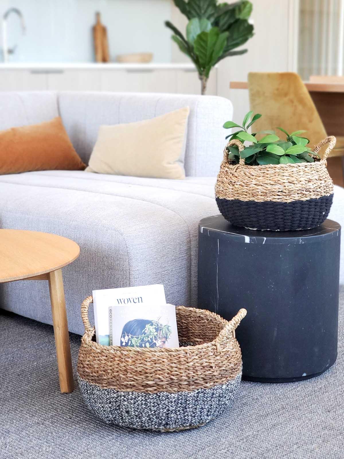 Set of two woven floor baskets in black and gray, one with plant, modern living room setting