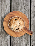 crumb-topped muffin in white paper cup on round wooden serving board on rustic wooden table