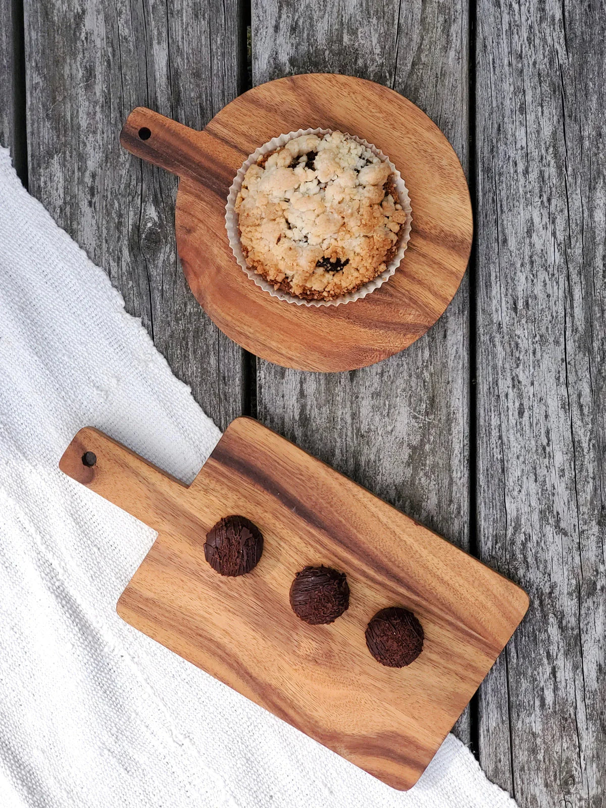 Wooden boards on weathered gray table with crumbly muffin and three chocolate truffles on white cloth