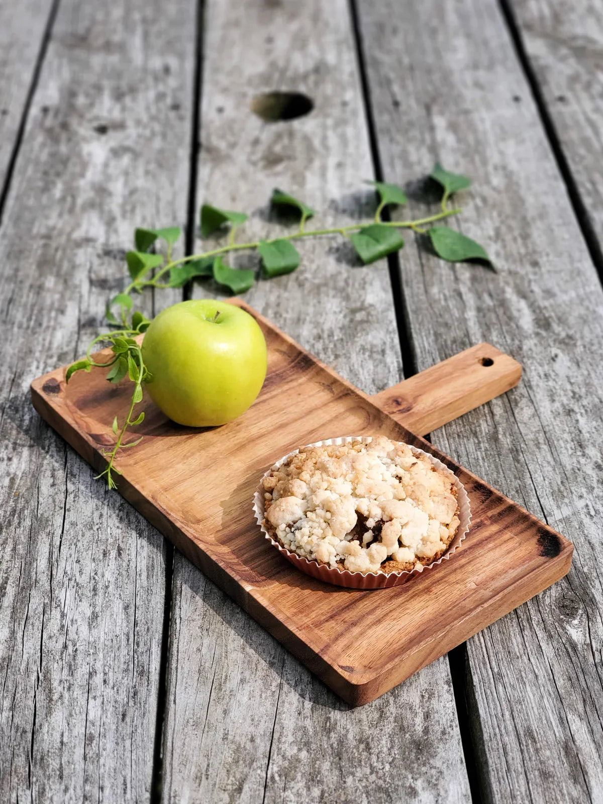 Wooden serving board with a green apple and a crumb-topped dessert placed on weathered wooden surface