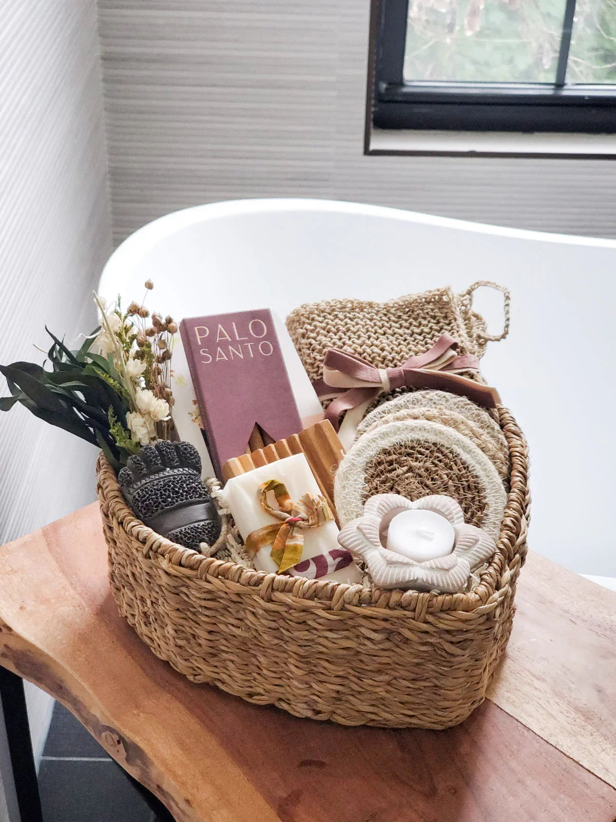 Heart-shaped wicker gift basket with Palo Santo, soaps, woven scrubbers, and dried flowers on wooden table