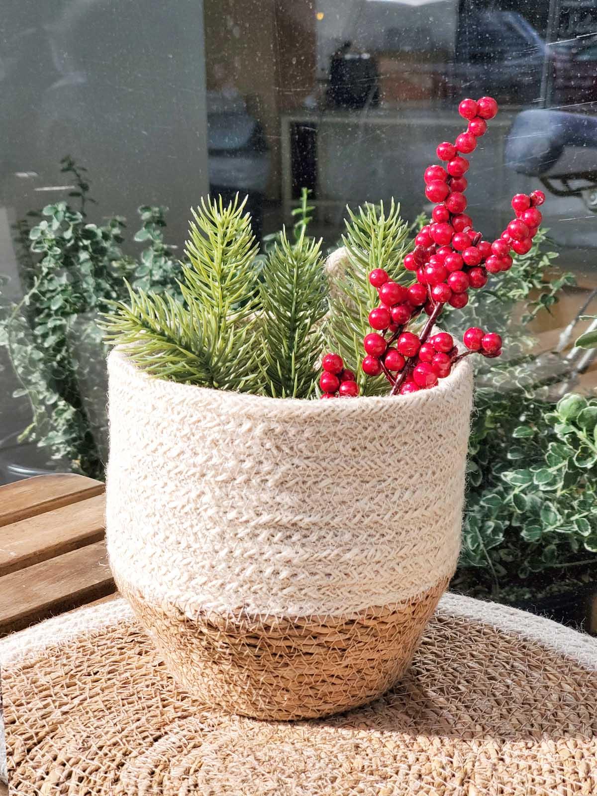Natural woven basket with festive faux pine branches and red berries, on display at Qu!rk Boutique.