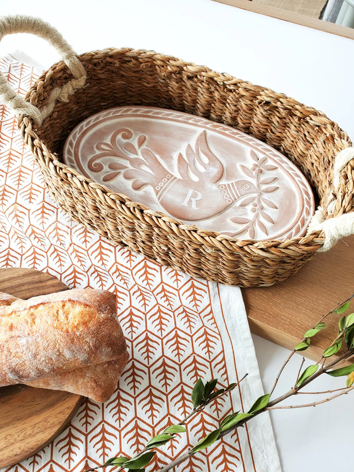 Woven bread warmer basket with personalized ceramic insert featuring bird and olive branch design on patterned cloth