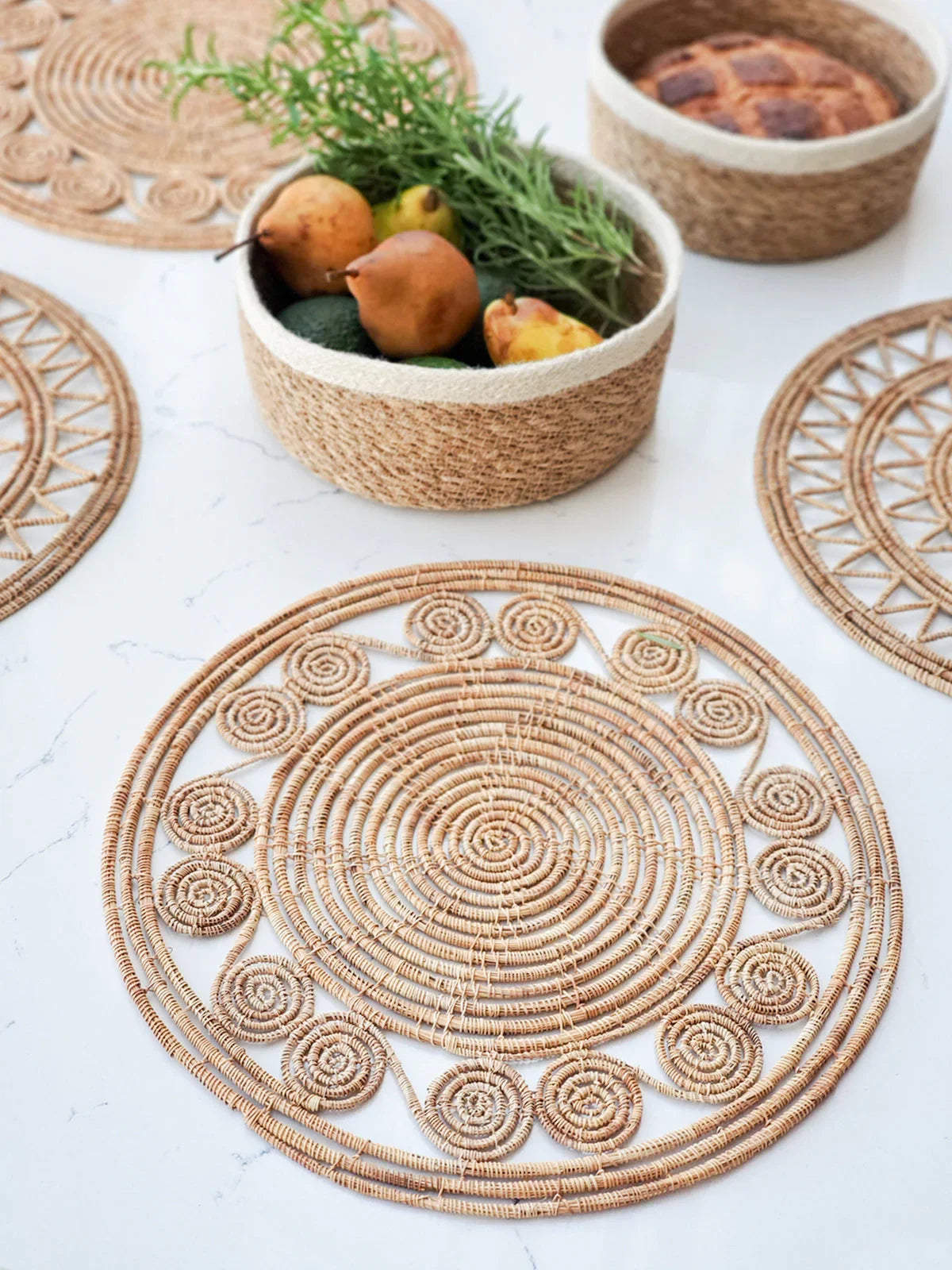 woven palm fiber placemats with circular patterns on white surface, natural fiber fruit baskets with pears and herbs