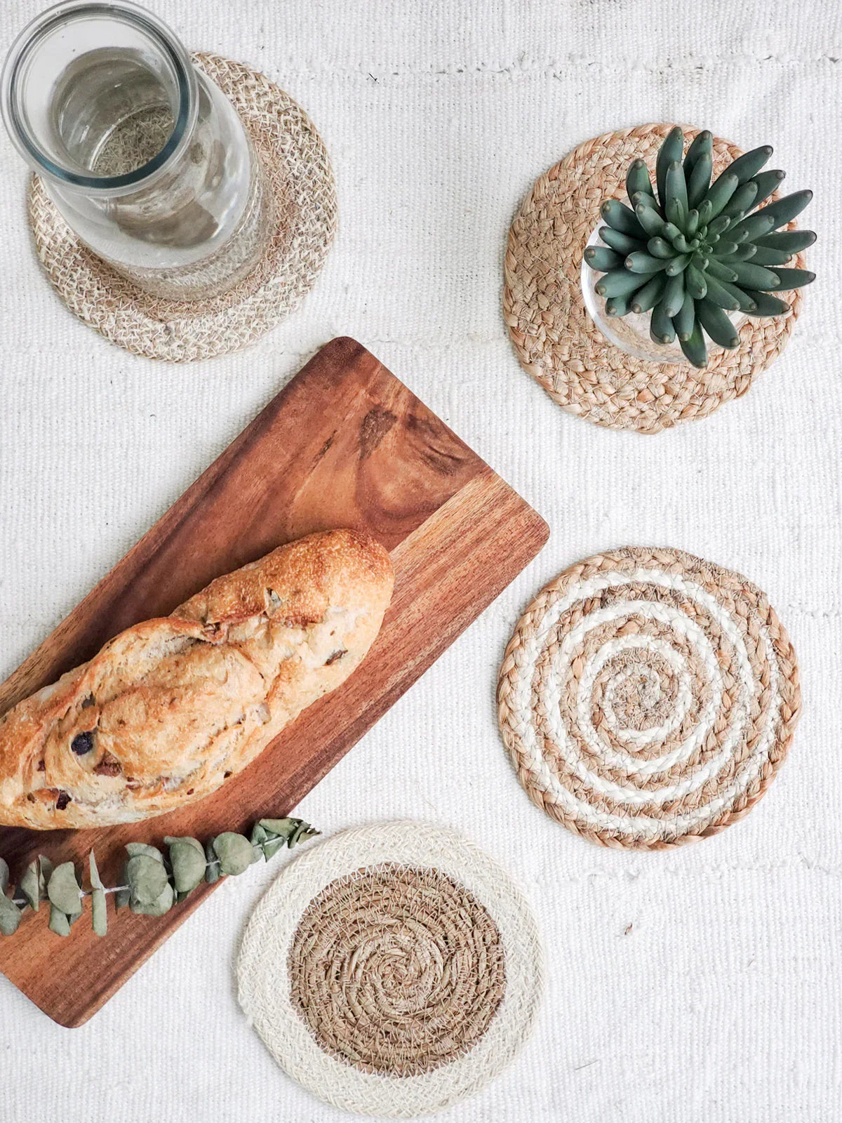 Rustic bread on wooden cutting board with glass carafe and succulent on woven coasters